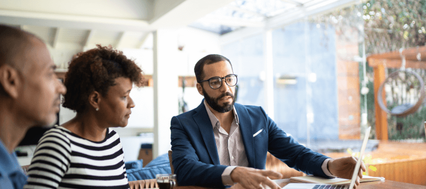 A real estate agent shows a laptop screen to a couple.