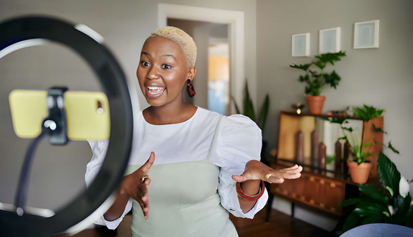 A woman filming a vlog inside a home using her iPhone and a ring light.