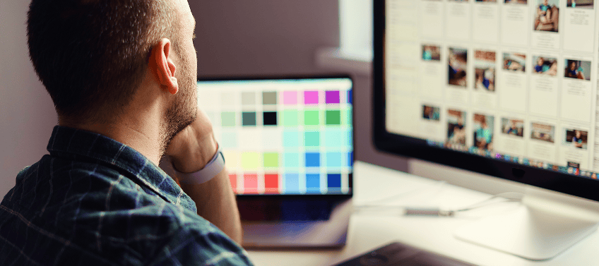 A designer selecting colors and reviewing images for a custom website design on dual monitors.